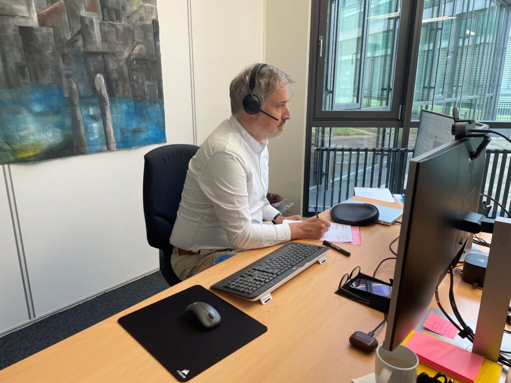 Stefan Wirz an seinem Arbeitstisch, umgeben von Bildschirmen und Schreibunterlagen