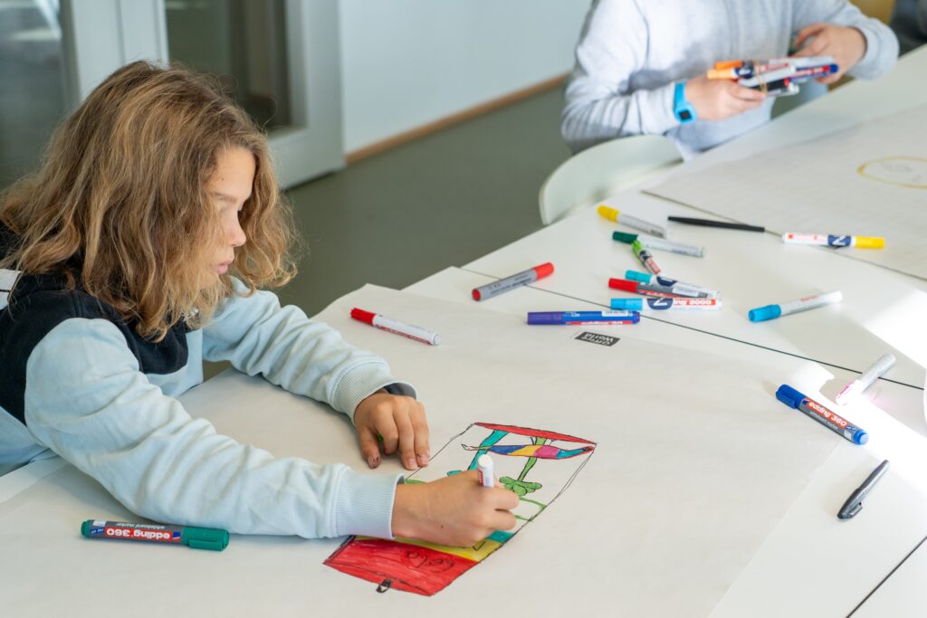 Schüler beim Gestalten eines Plakats mit Stift und Papier.